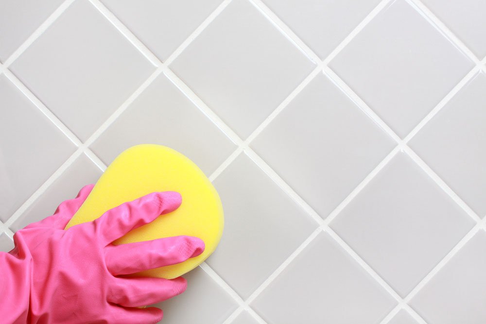 Hand with glove clearning the bathroom tiles